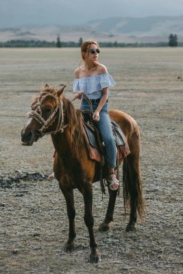 A woman in a bardot top rides a horse through an open field, enjoying the countryside view.
